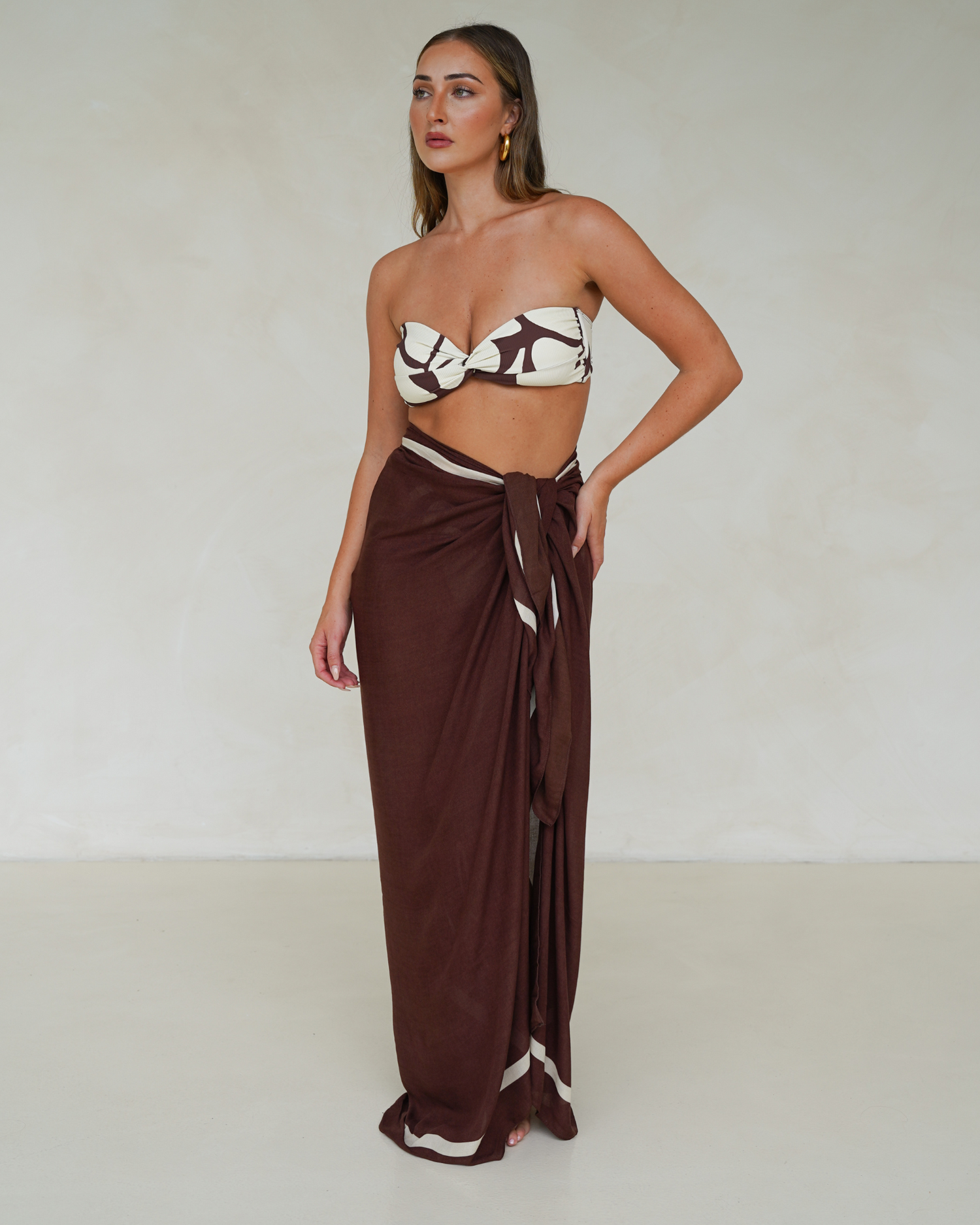 Model wearing chocolate brown rayon sarong with cream trim, styled over matching printed bandeau bikini – Ochre Lane resortwear