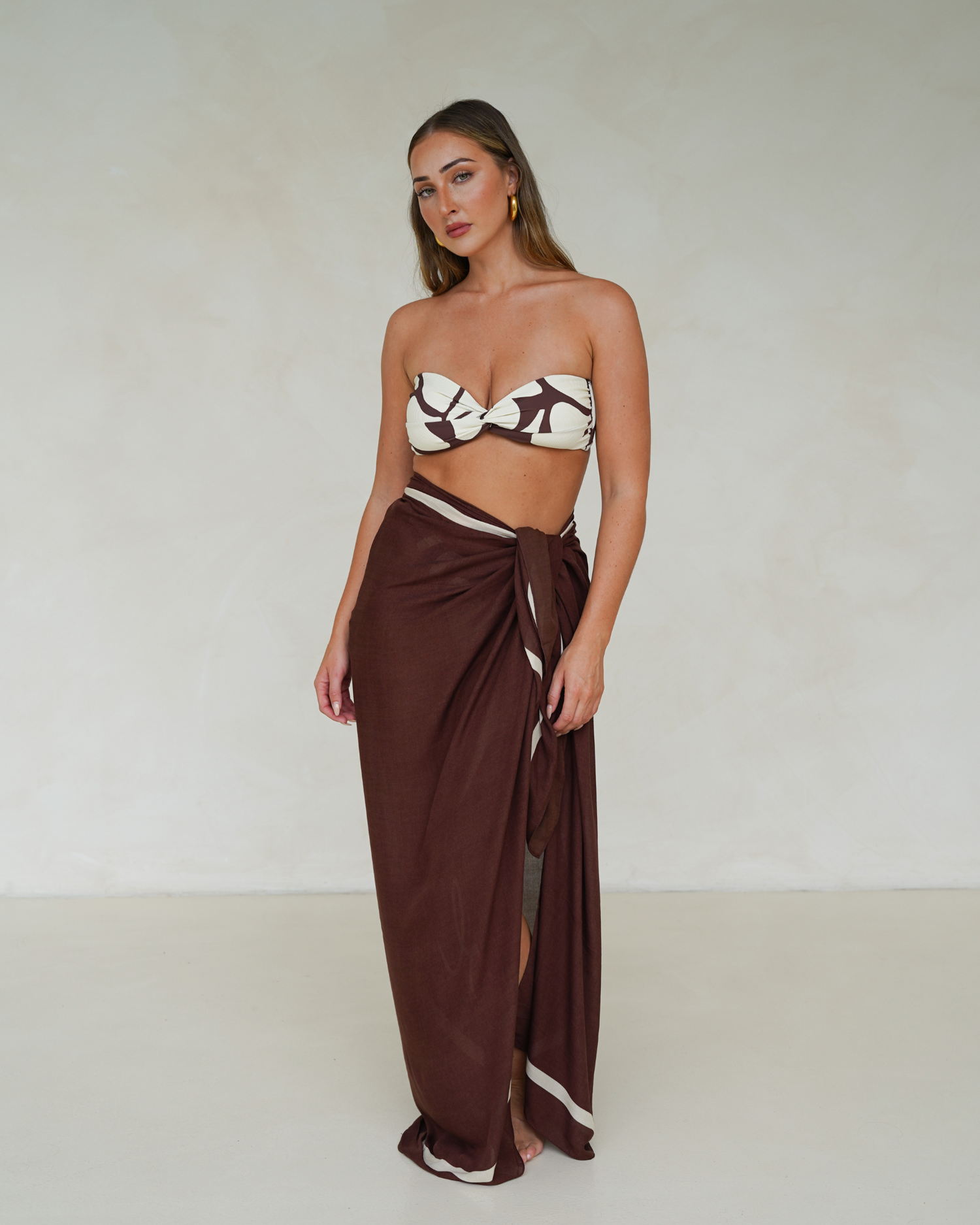 Model wearing chocolate brown rayon sarong with cream trim, styled over matching printed bandeau bikini – Ochre Lane resortwear