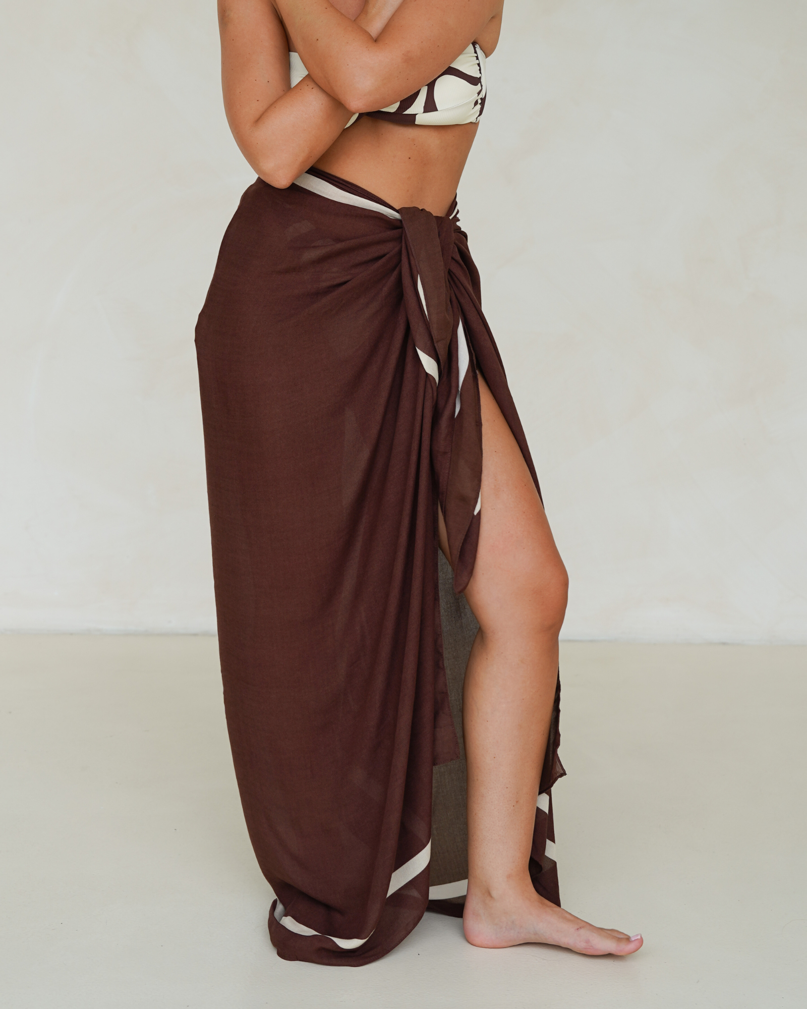 Model wearing chocolate brown rayon sarong with cream trim, styled over matching printed bandeau bikini – Ochre Lane resortwear