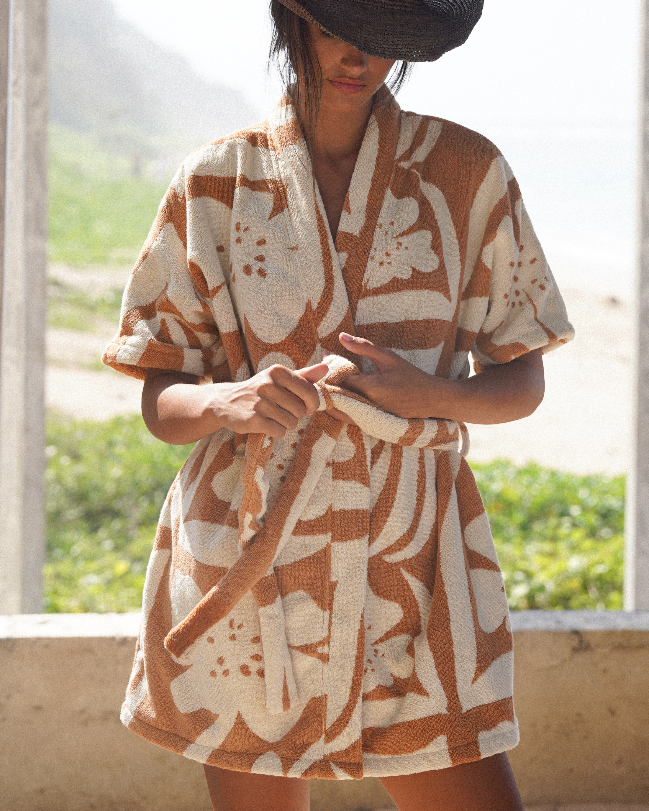 Model wearing the Sienna cotton towelling robe in beige and light caramel floral print by Ochre Lane, designed with a relaxed resort fit, short hemline, wide sleeves, and a self-tie waist—ideal for beach layering or lounging.