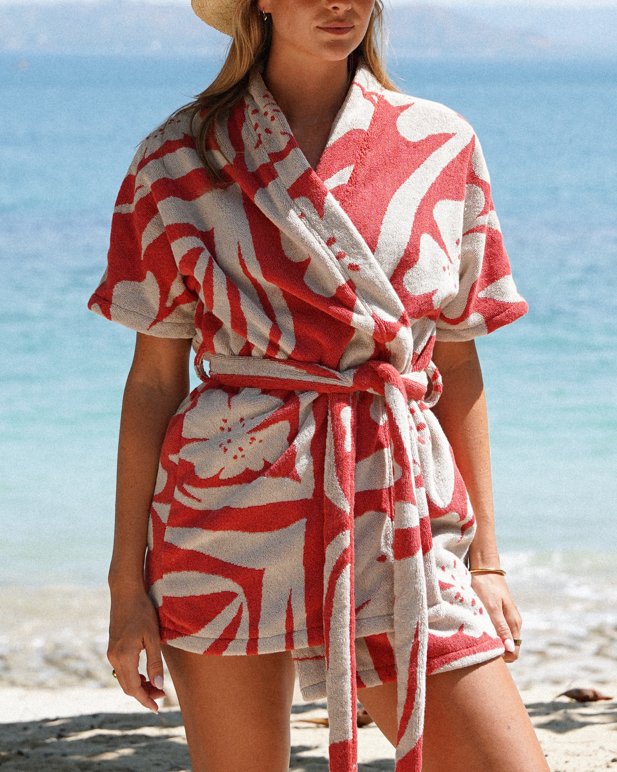 Model wearing the Solana cotton towelling robe in red watermelon floral print by Ochre Lane, featuring a short resort-style silhouette, tie waist, and wide sleeves—perfect for beach days or poolside layering.