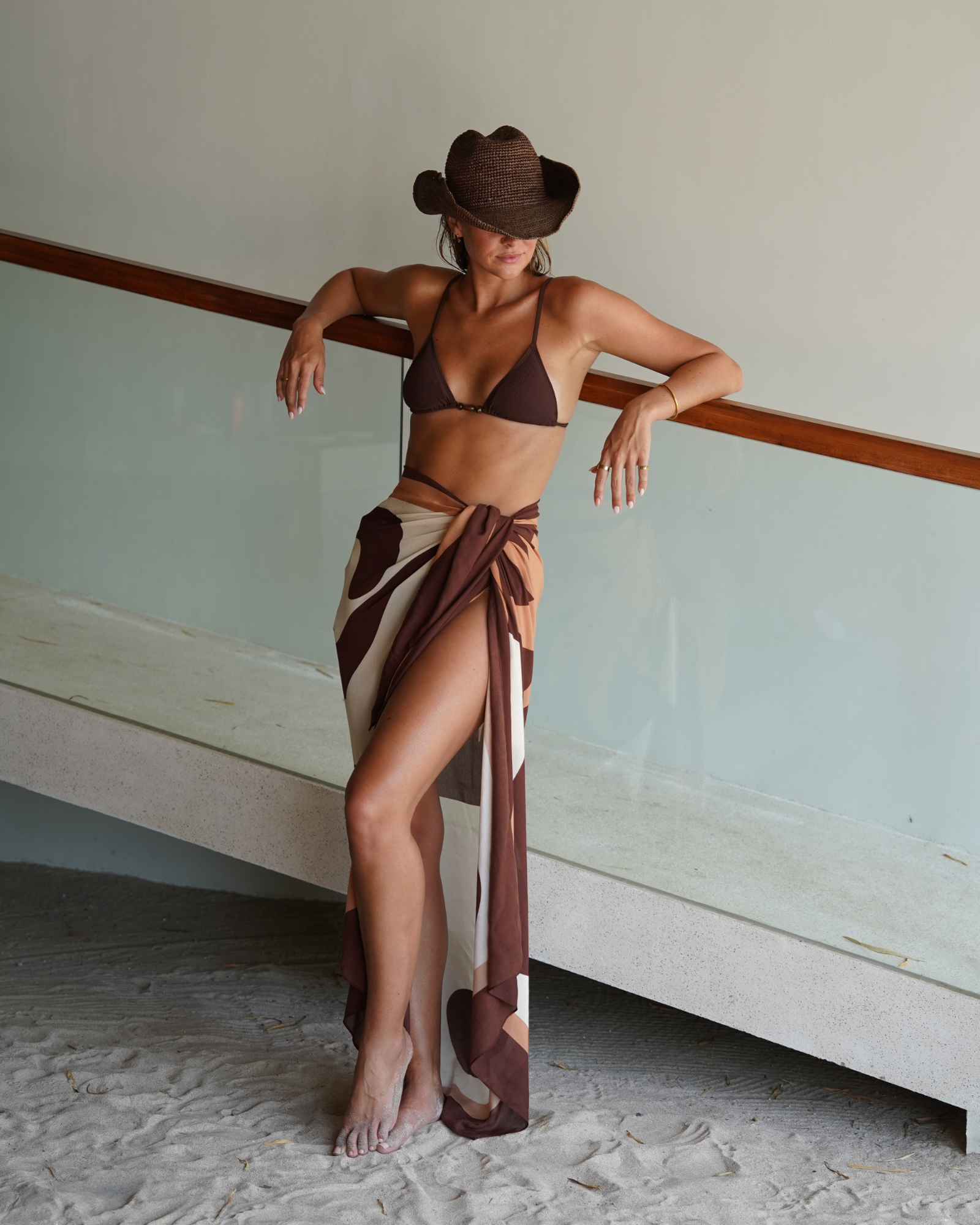 Woman wearing abstract floral sarong in chocolate tones styled as a skirt with neutral bikini top.