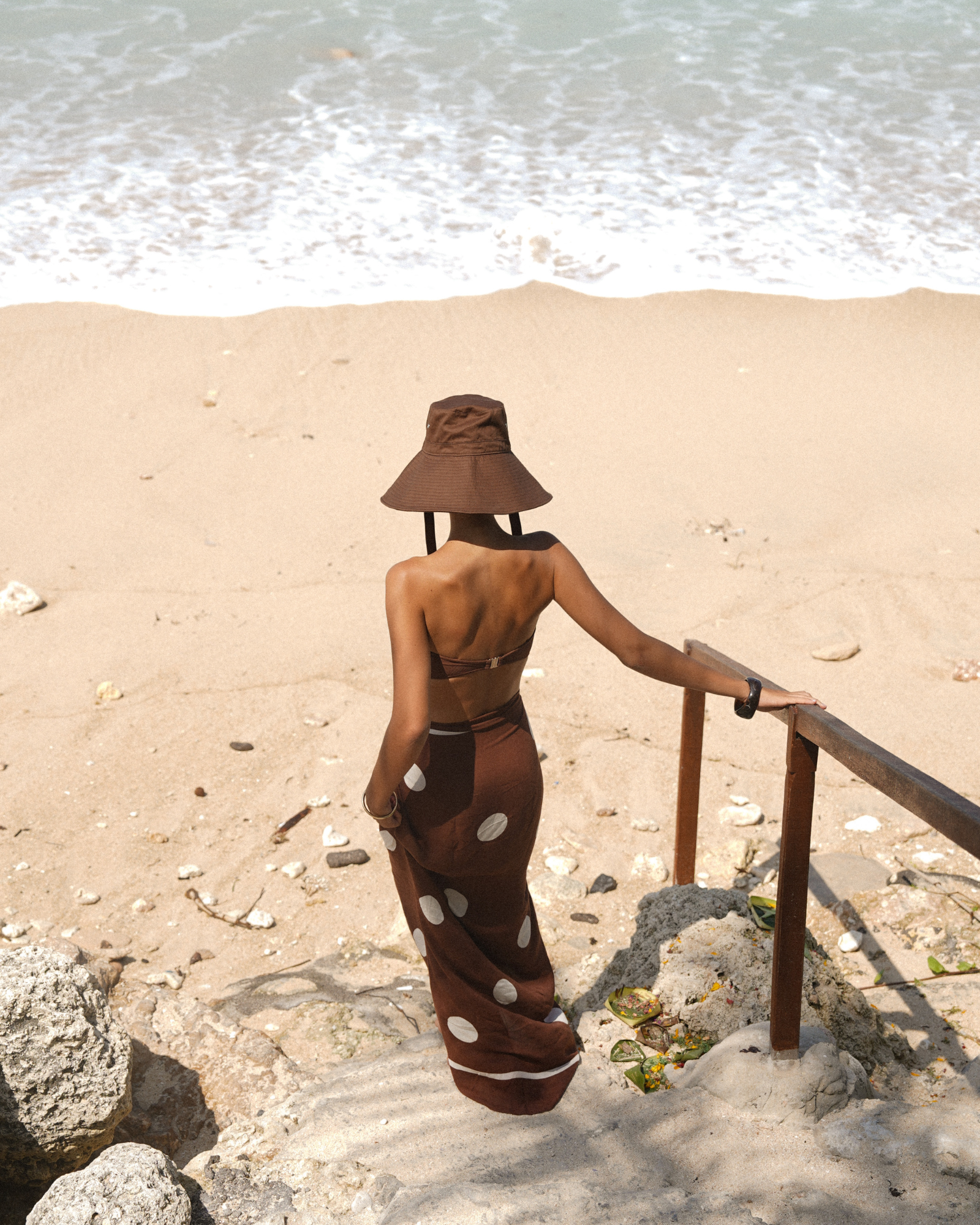 Chocolate pareo sarong with bold white dot print, worn over swimwear for a resort-ready look.
