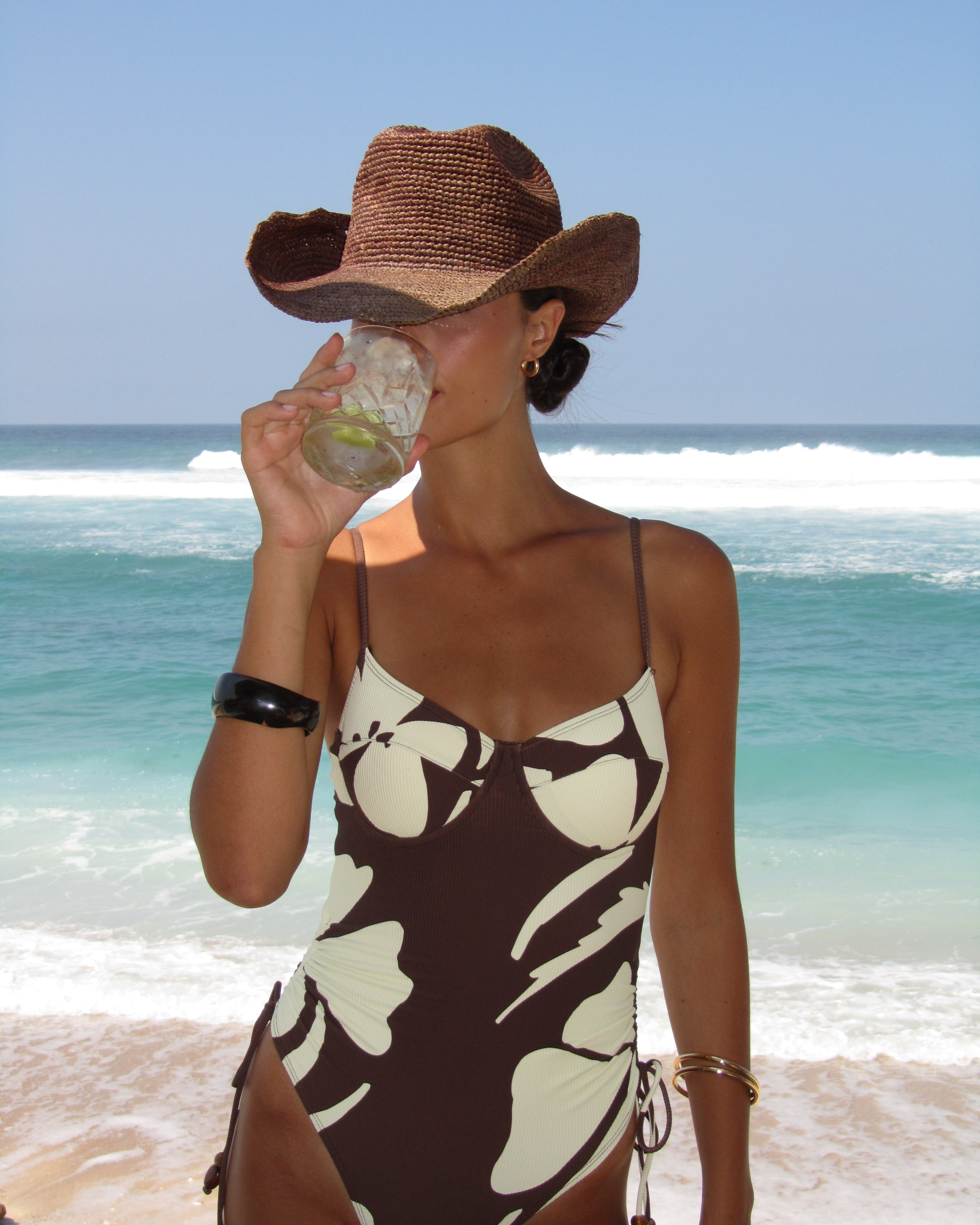 Printed ribbed one piece swimsuit in dark brown with ivory hibiscus and adjustable string sides.