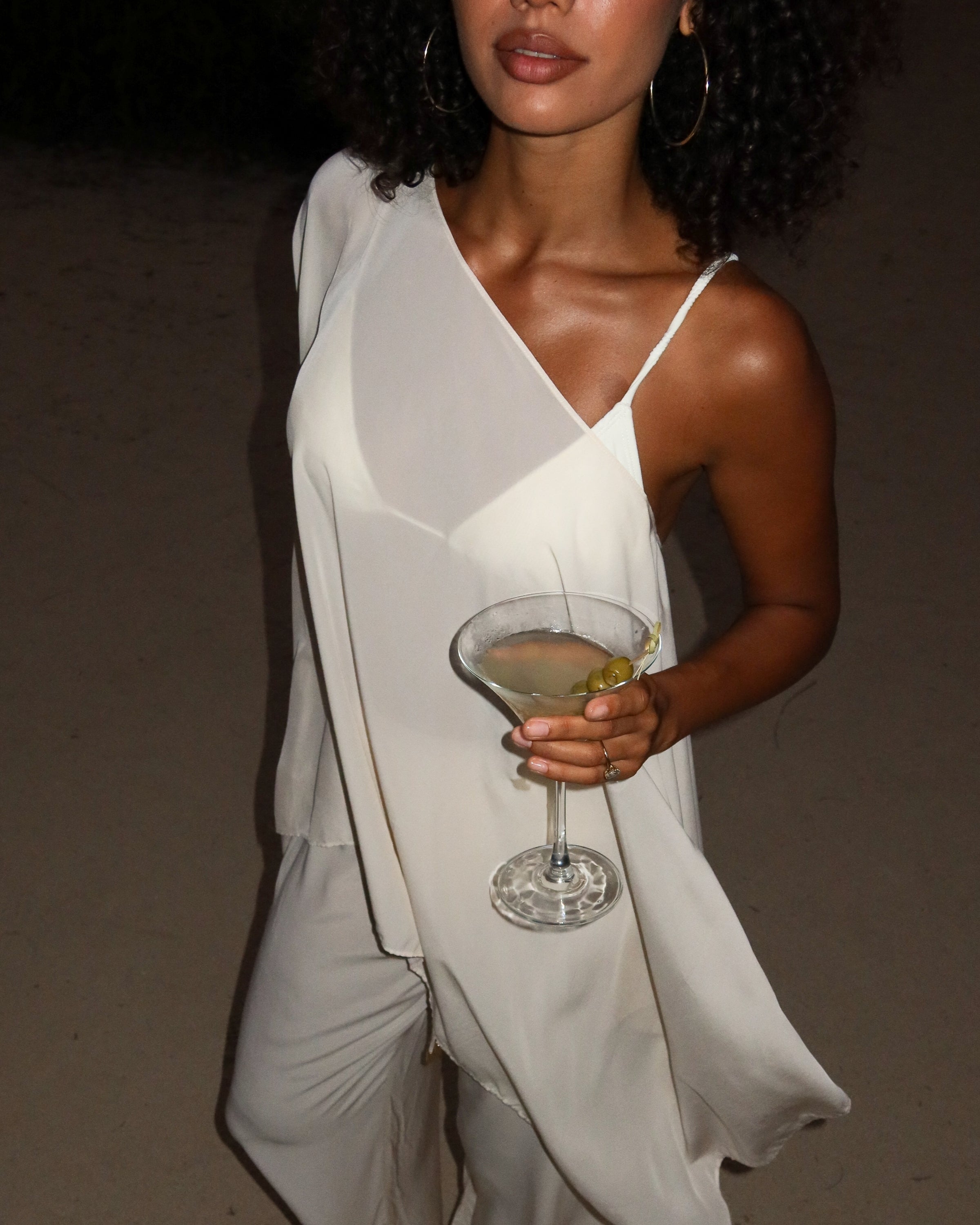 Close view of a sheer ivory resort cape draped one-shoulder over a slip and pants at dusk, cascading points