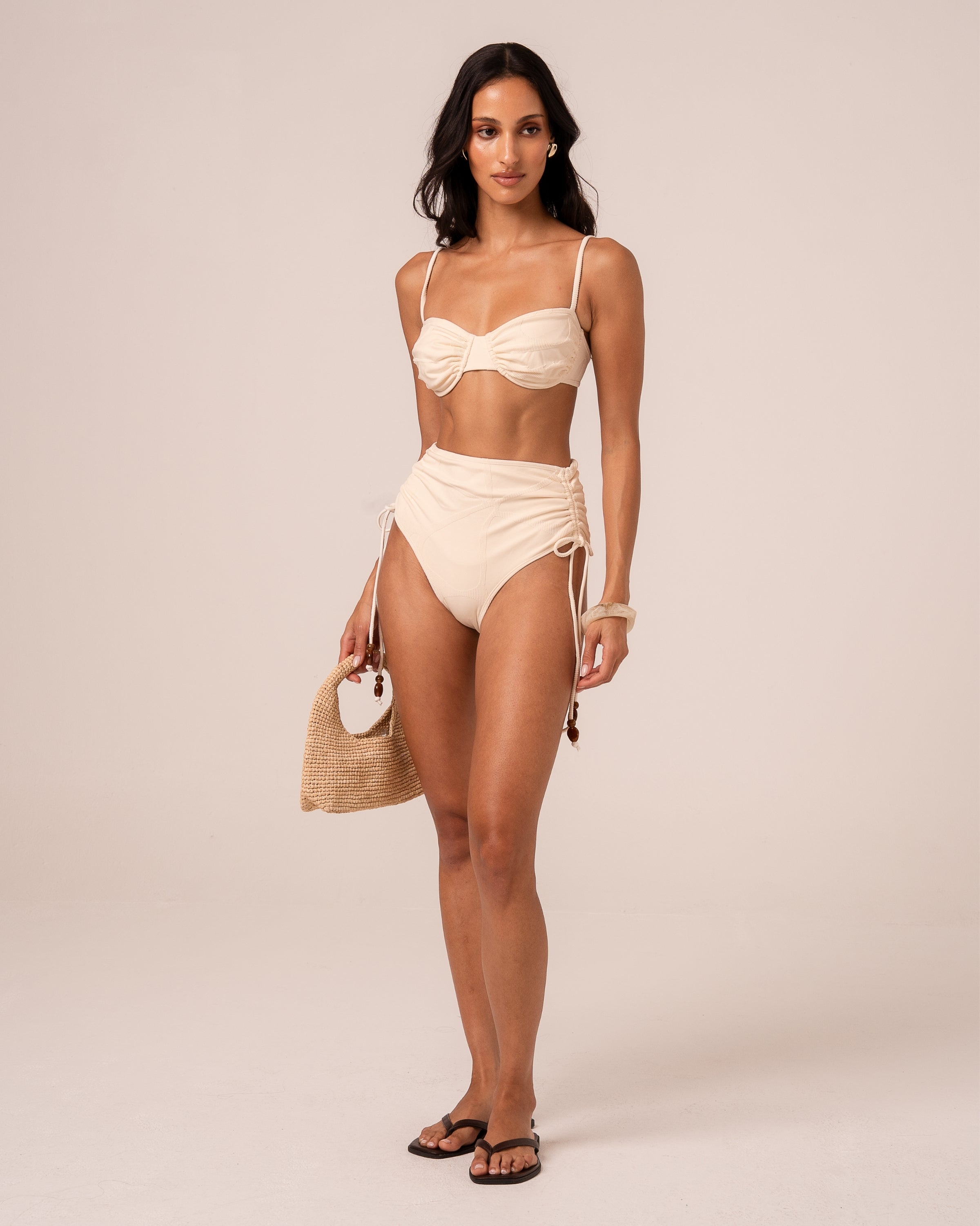 Model wearing an ivory soft cup bralette bikini top with ruched centre gathering, styled with a high waist bottom — studio front view