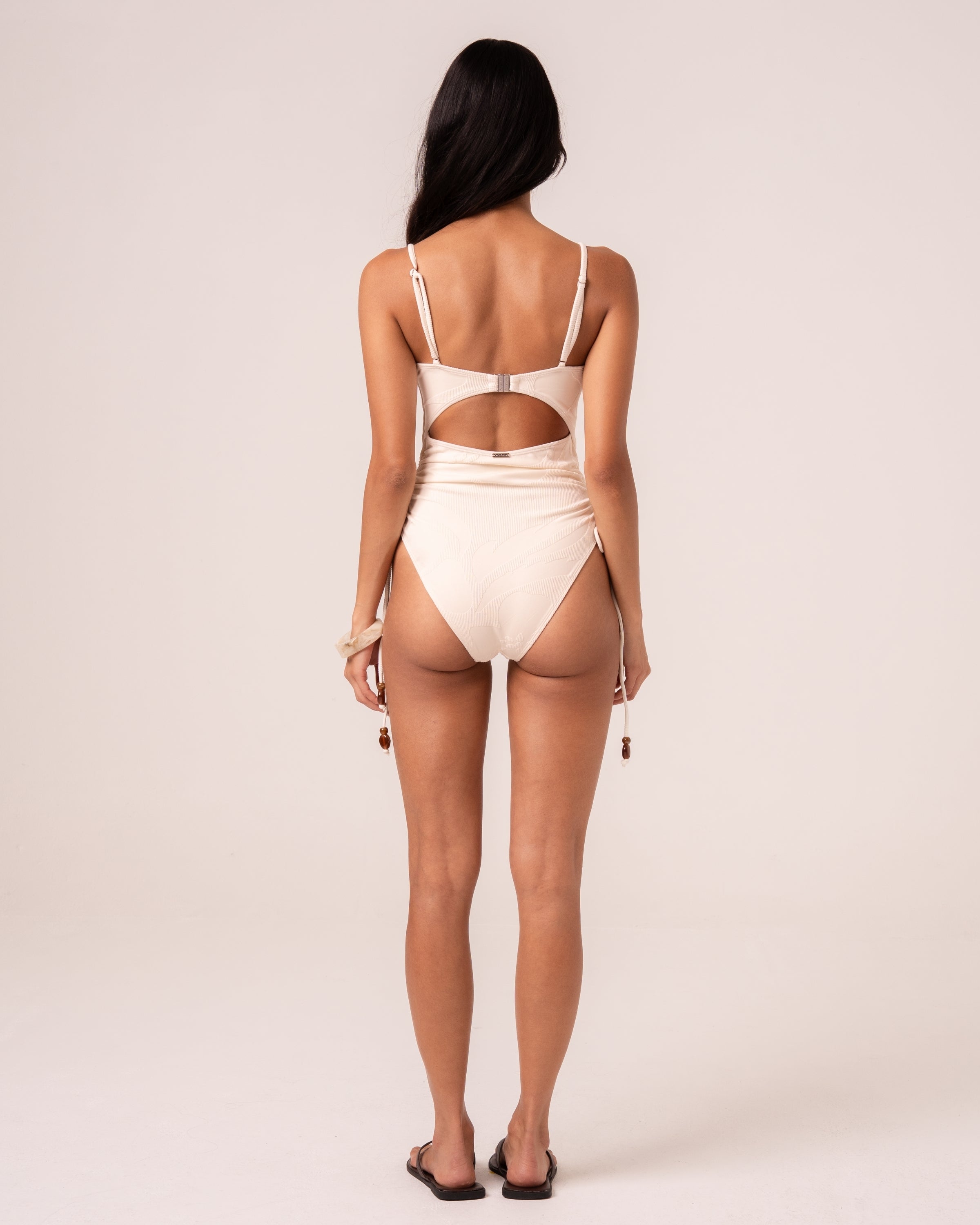 Back view of an ivory underwire one piece swimsuit showing the cut-out back and beaded adjustable side ties