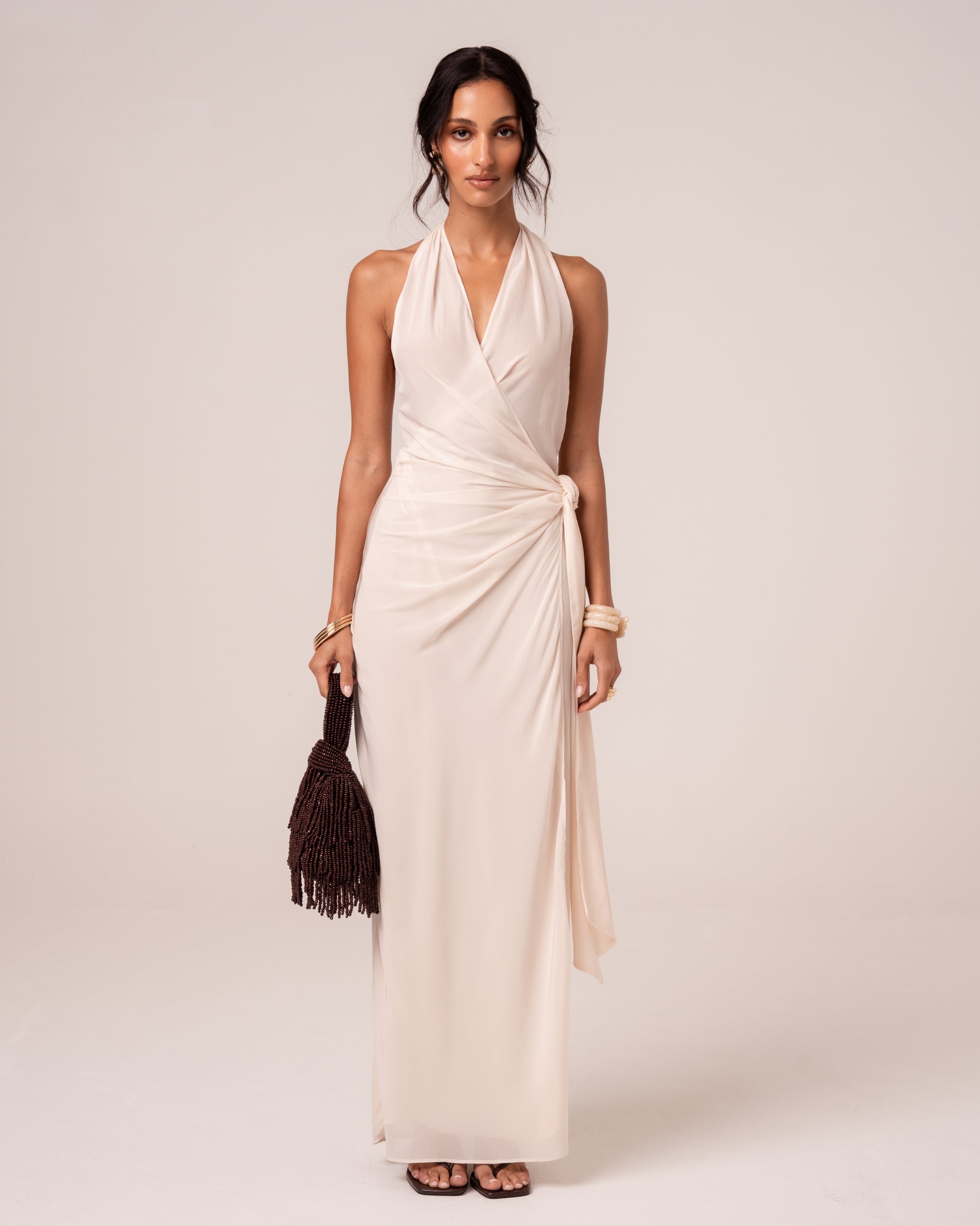 Front view of an ivory wrap maxi dress with draped side knot and floor-length column silhouette