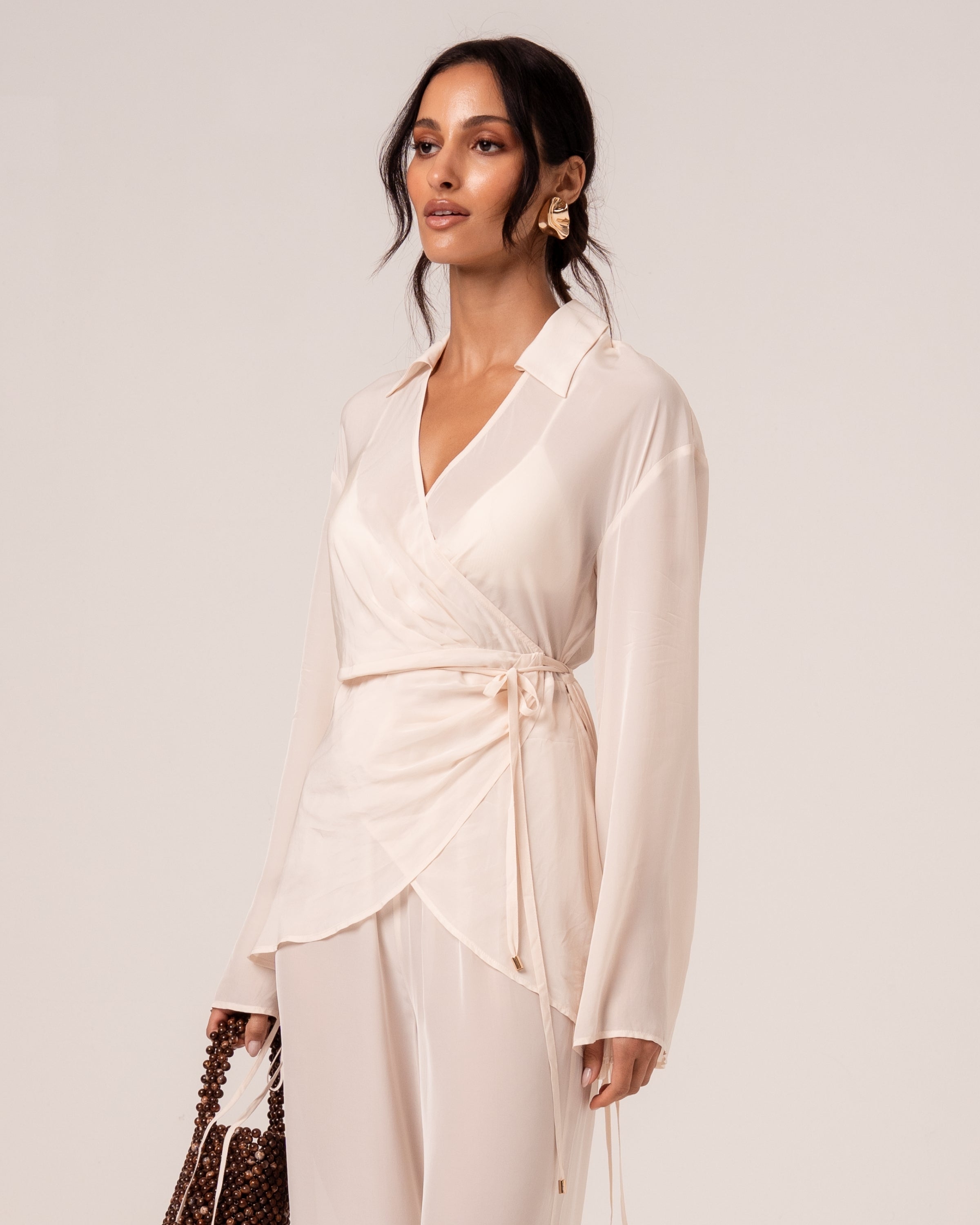 Close view of an ivory wrap shirt showing the V-neckline, relaxed collar and self-tie waist with gold-tipped ties