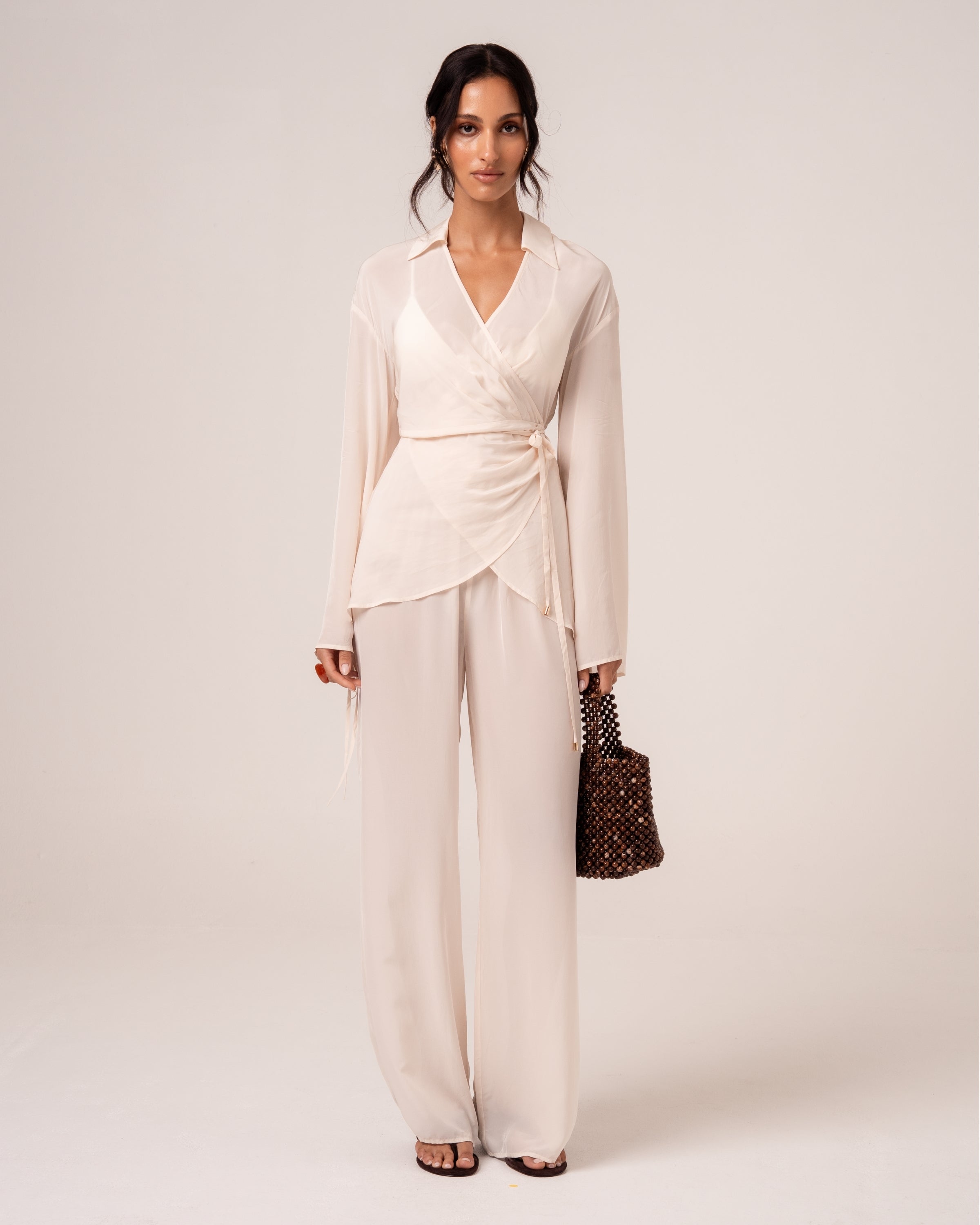 Model wearing an ivory viscose wrap shirt with self-tie waist and tulip hem over matching wide-leg resort pants, front view