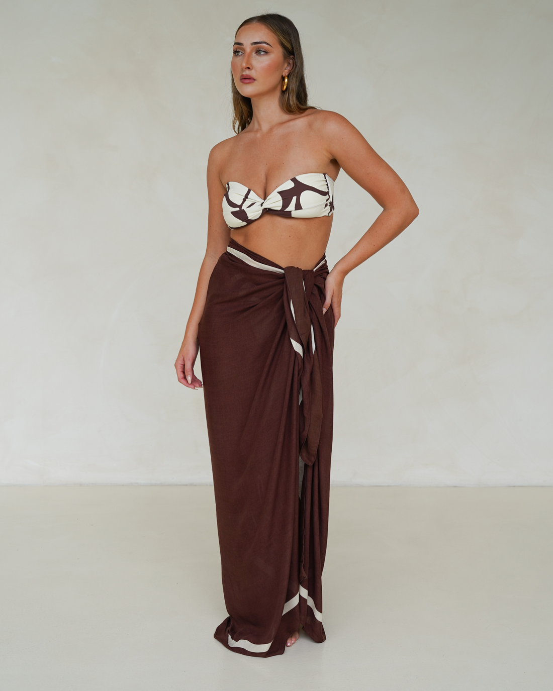 Model wearing chocolate brown rayon sarong with cream trim, styled over matching printed bandeau bikini – Ochre Lane resortwear
