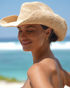 Natural raffia straw cowboy hat with wide curved brim, adjustable inner band, and branded metal logo detail.