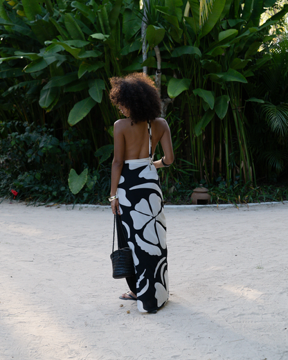 Back view of a model wearing a black and cream floral halter maxi dress with an open back, walking along a sandy path