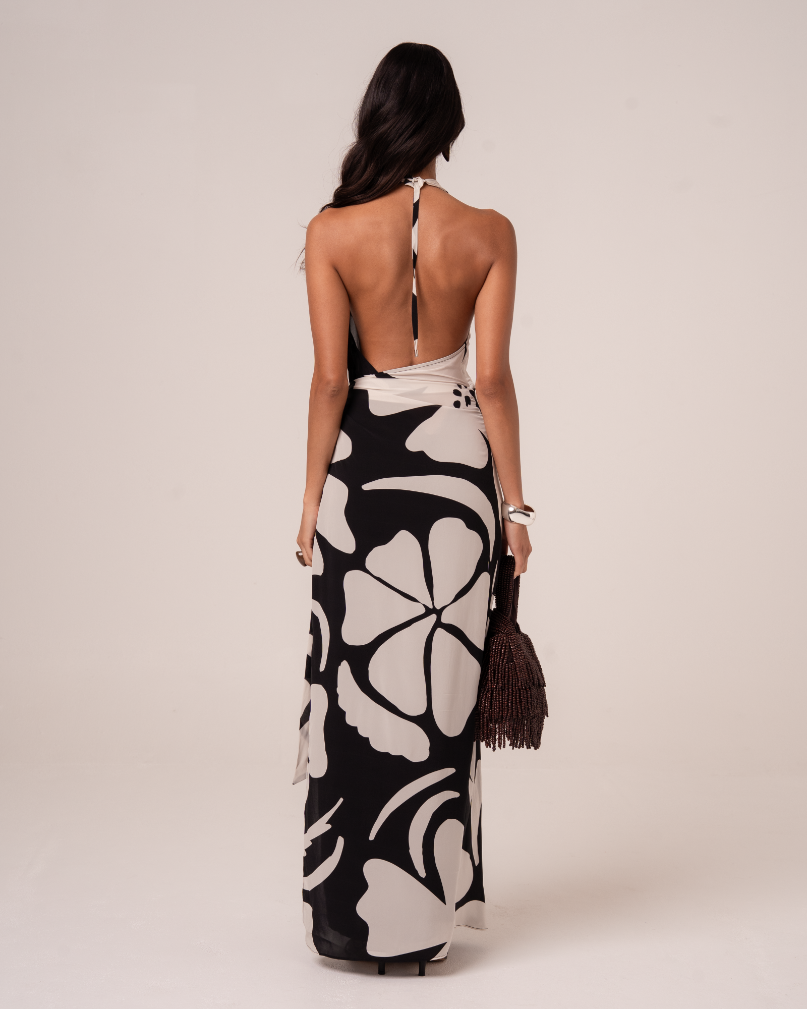 Back view of a black and cream floral halter maxi dress showing the open back and adjustable tie, studio view