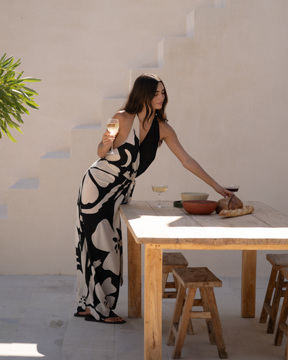 Side view of a model wearing a black and cream floral halter wrap maxi dress leaning over an outdoor table, styled for alfresco dining