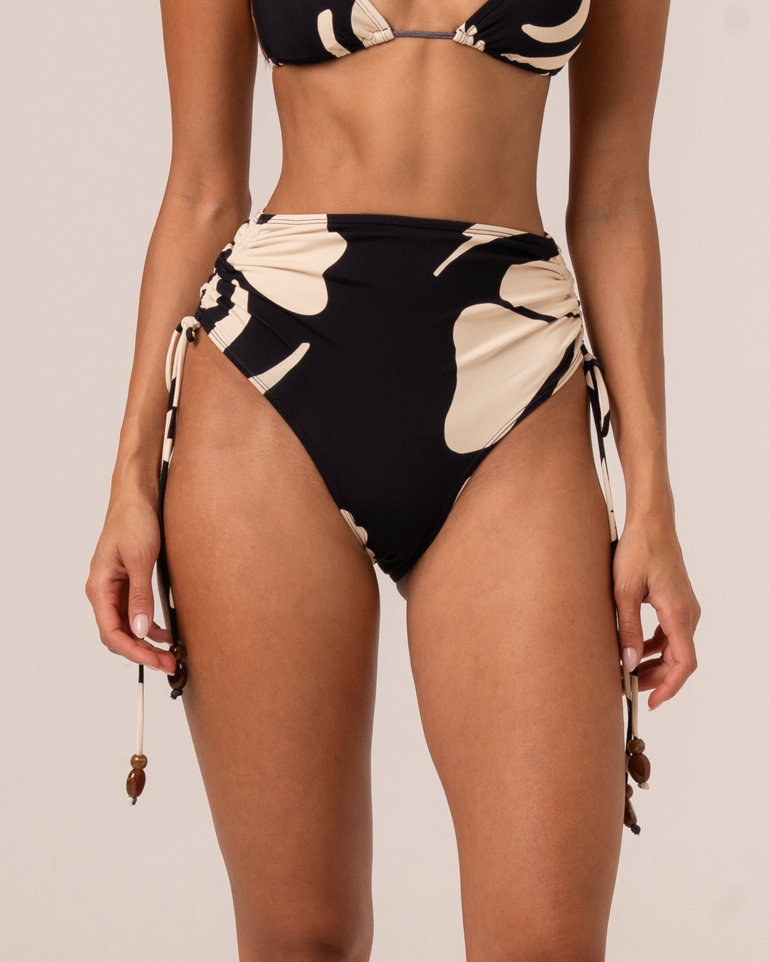 Close-up of black and cream floral print high waist tie side bikini bottom with beaded ties, worn with matching triangle top