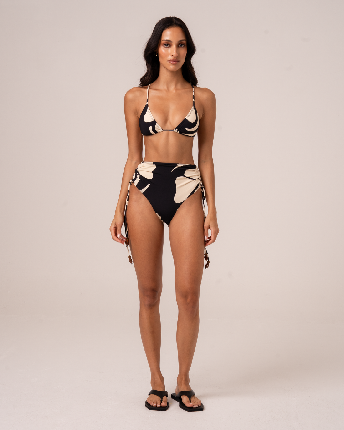 Woman wearing black and cream floral print high waist tie side bikini bottom and matching triangle top, front view