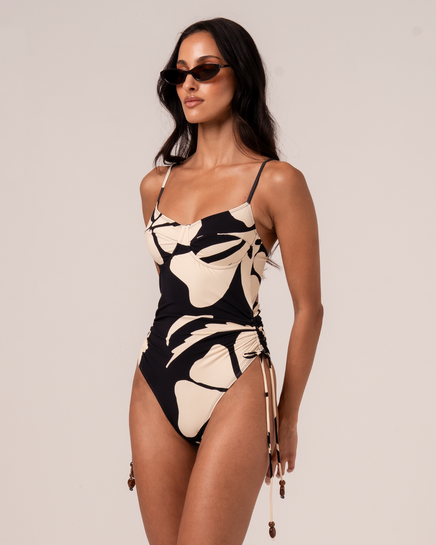 Side view of black and cream botanica floral print thin strap underwire one-piece swimsuit with ruched drawstring waist
