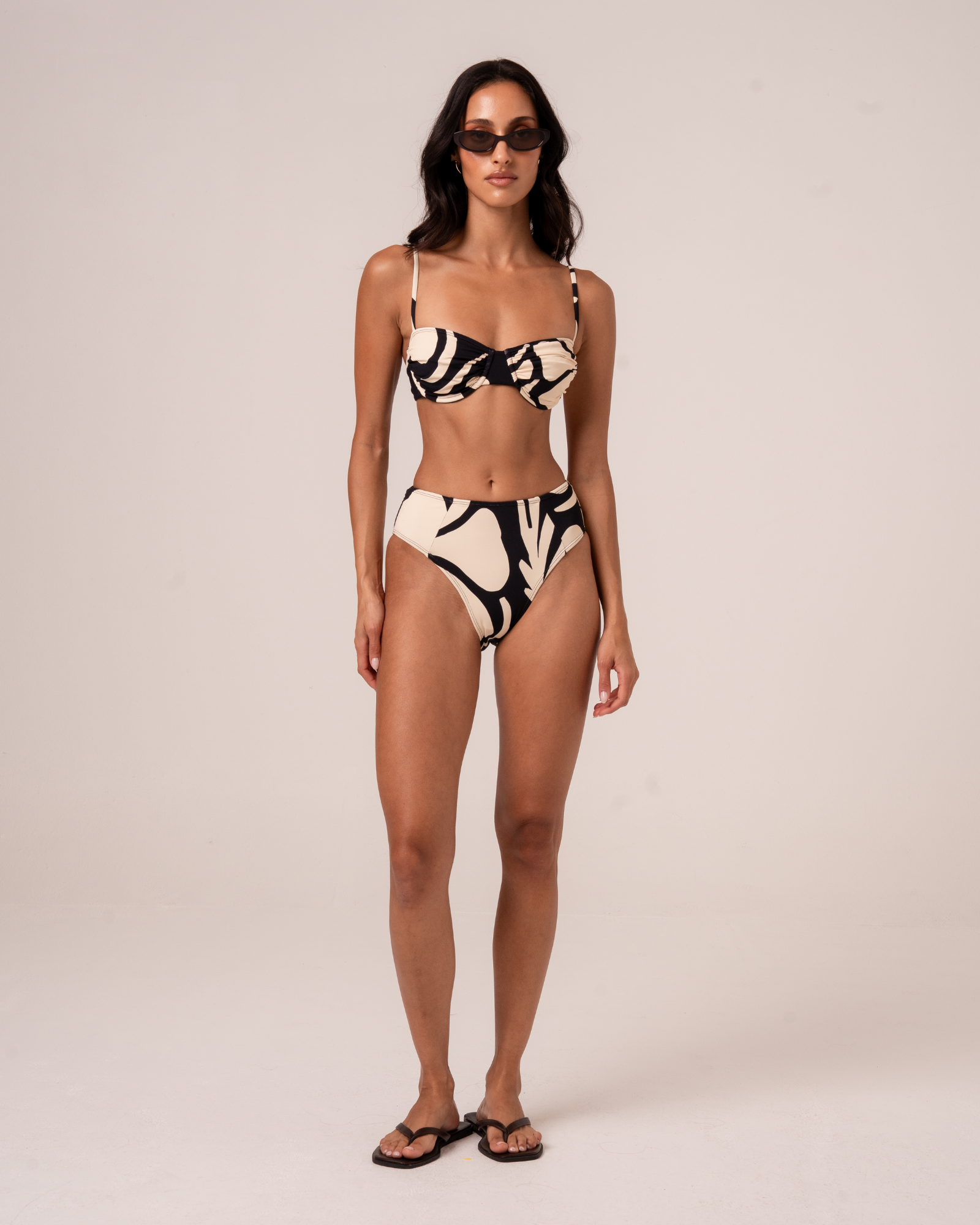 Full-length front view of botanica print mid-rise bikini bottom in black and cream, styled with a ruched bandeau top