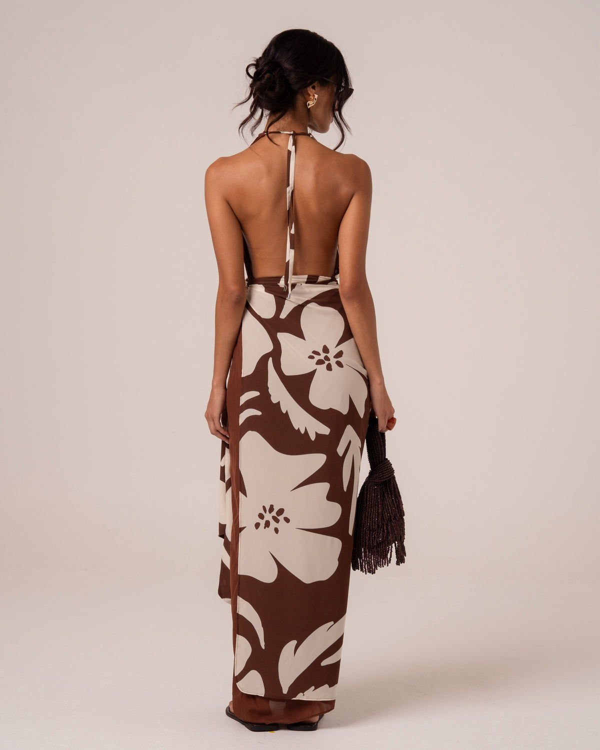 Back view of a brown and cream floral halter maxi dress showing the deep open back and halter tie