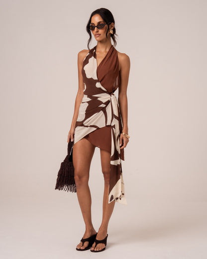 Back view of a brown and cream floral halter mini dress showing the open back and trailing side tie