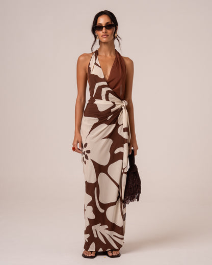 Model wearing a brown and cream floral halter wrap maxi dress with a plunging neckline and knotted side tie, studio front view