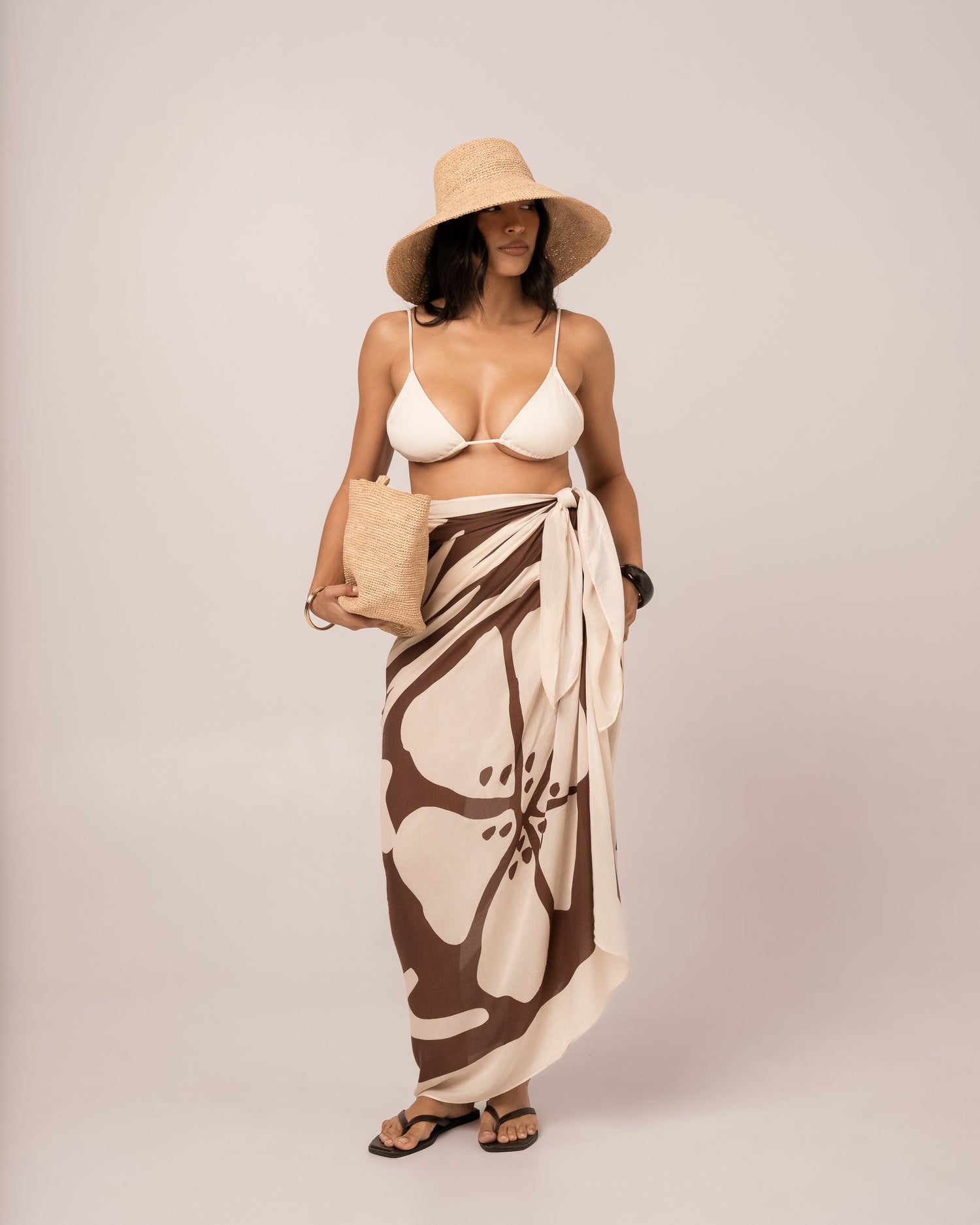 Ibisco Sarong in brown and ivory hibiscus print worn as a wrap skirt over an ivory bikini, full-length studio front view