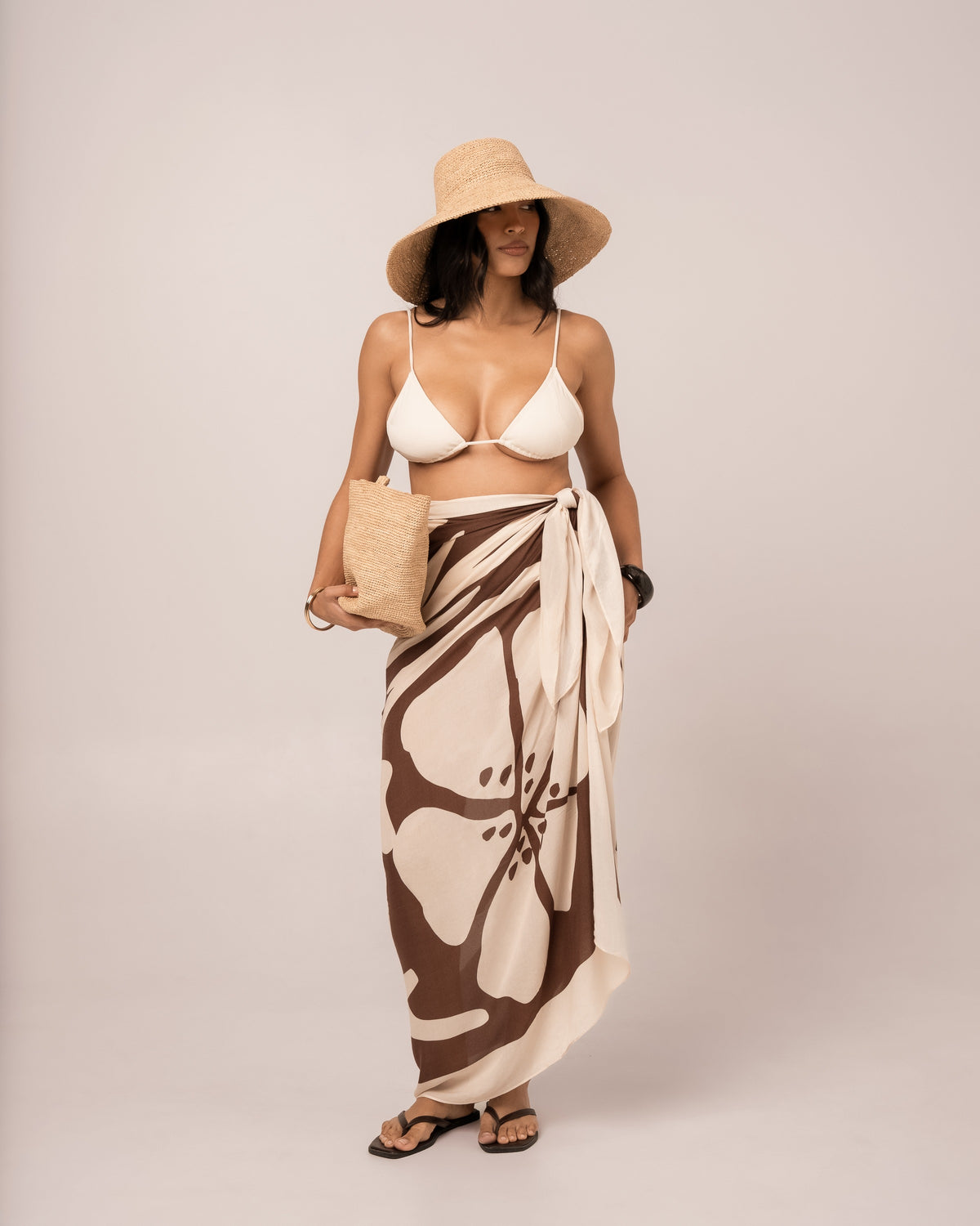 Ibisco Sarong in brown and ivory hibiscus print worn as a wrap skirt over an ivory bikini, full-length studio front view
