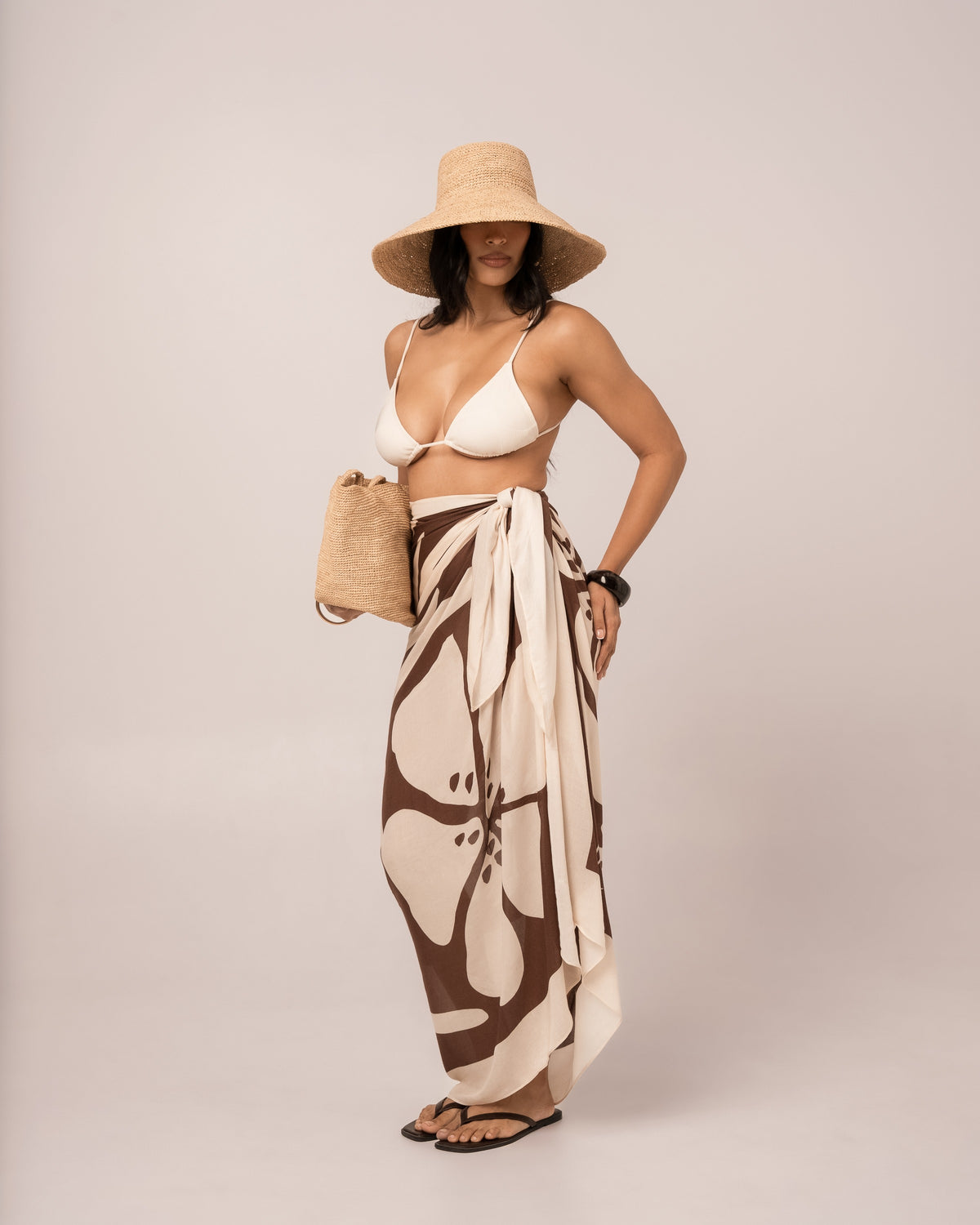 Brown floral Ibisco Sarong styled as a maxi wrap skirt over swimwear, relaxed hand-on-hip resort pose