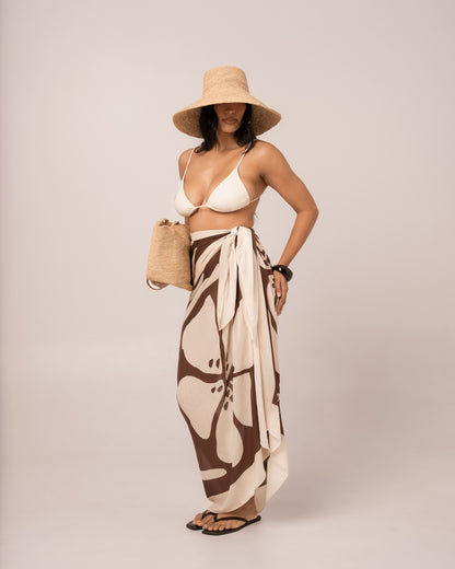 Brown floral Ibisco Sarong styled as a maxi wrap skirt over swimwear, relaxed hand-on-hip resort pose