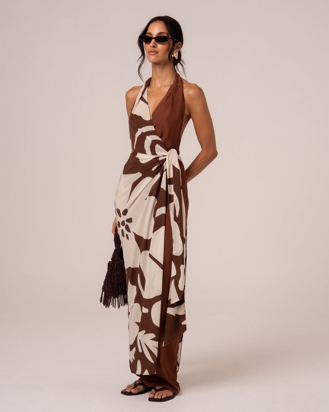 Side view of a brown and cream floral halter wrap maxi dress with a cascading waist tie drape, studio setting