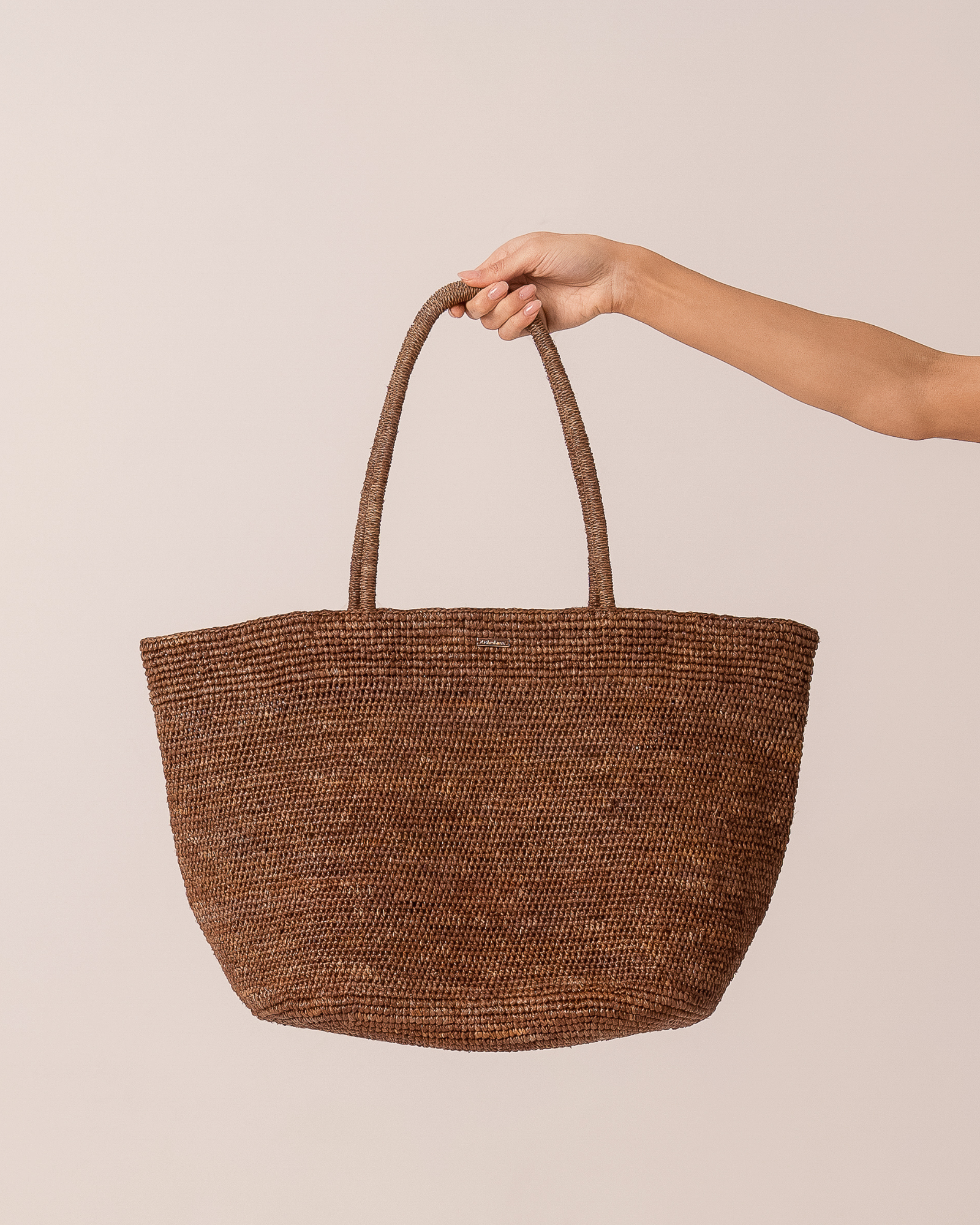 Brown woven raffia maxi tote bag held up against a plain studio background, full front view