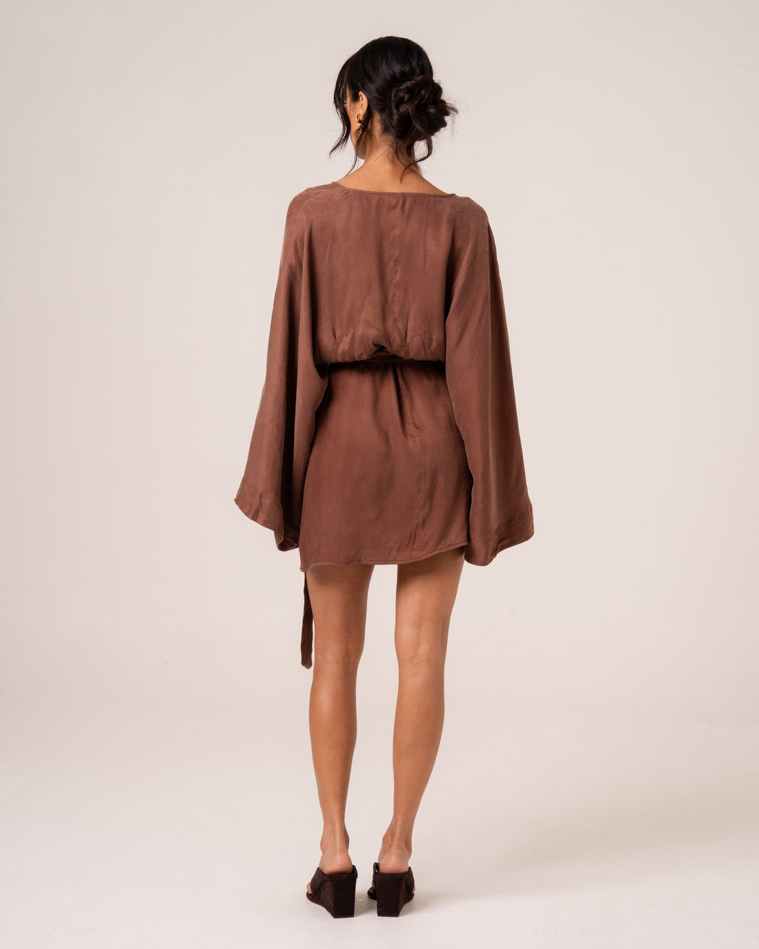 Back view of a chocolate brown batwing wrap mini dress showing the clean back and wide relaxed sleeves