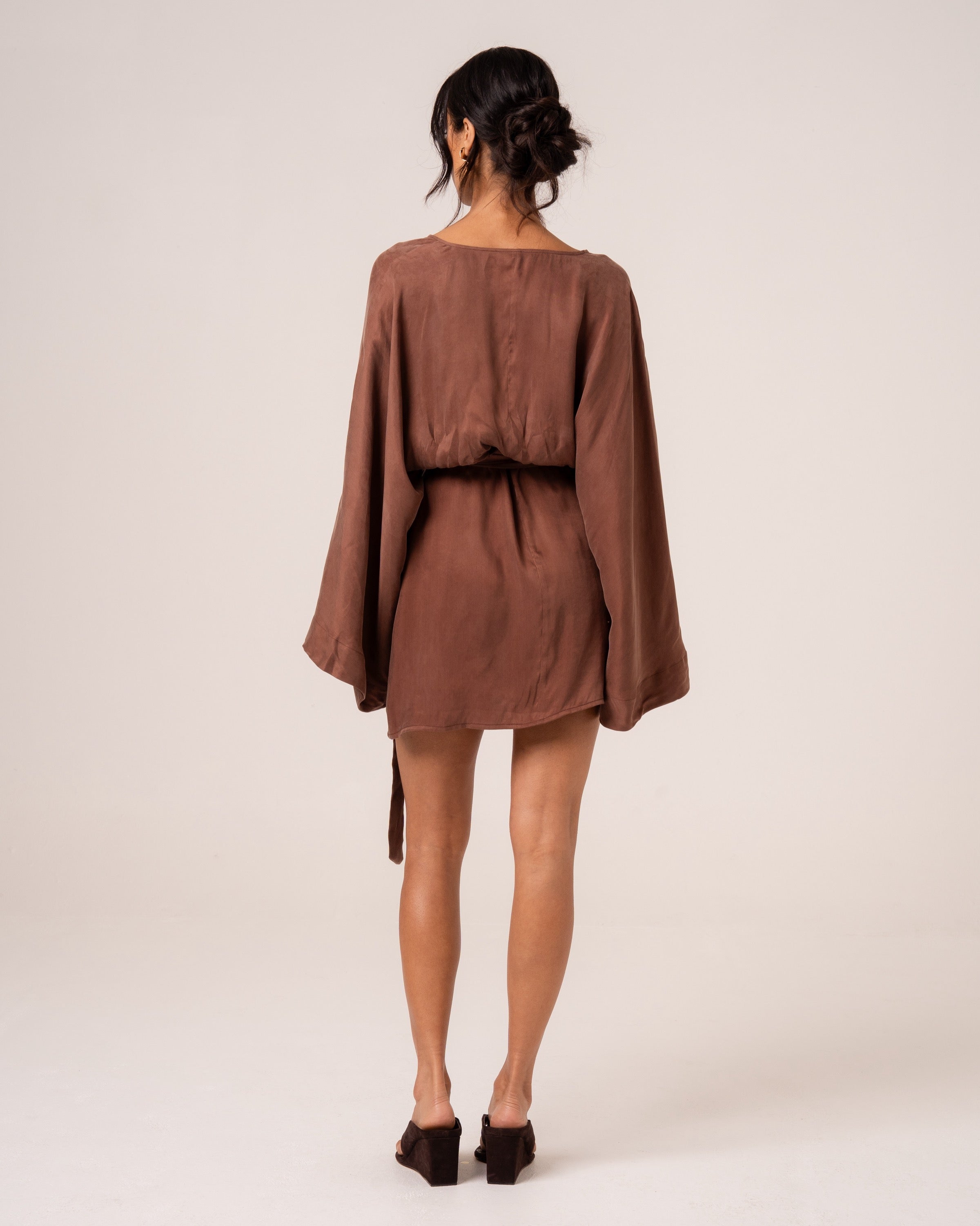 Back view of a chocolate brown batwing wrap mini dress showing the clean back and wide relaxed sleeves