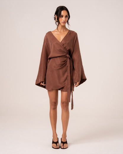 Model wearing a chocolate brown batwing wrap mini dress with a deep V-neckline and wide sleeves, studio front view