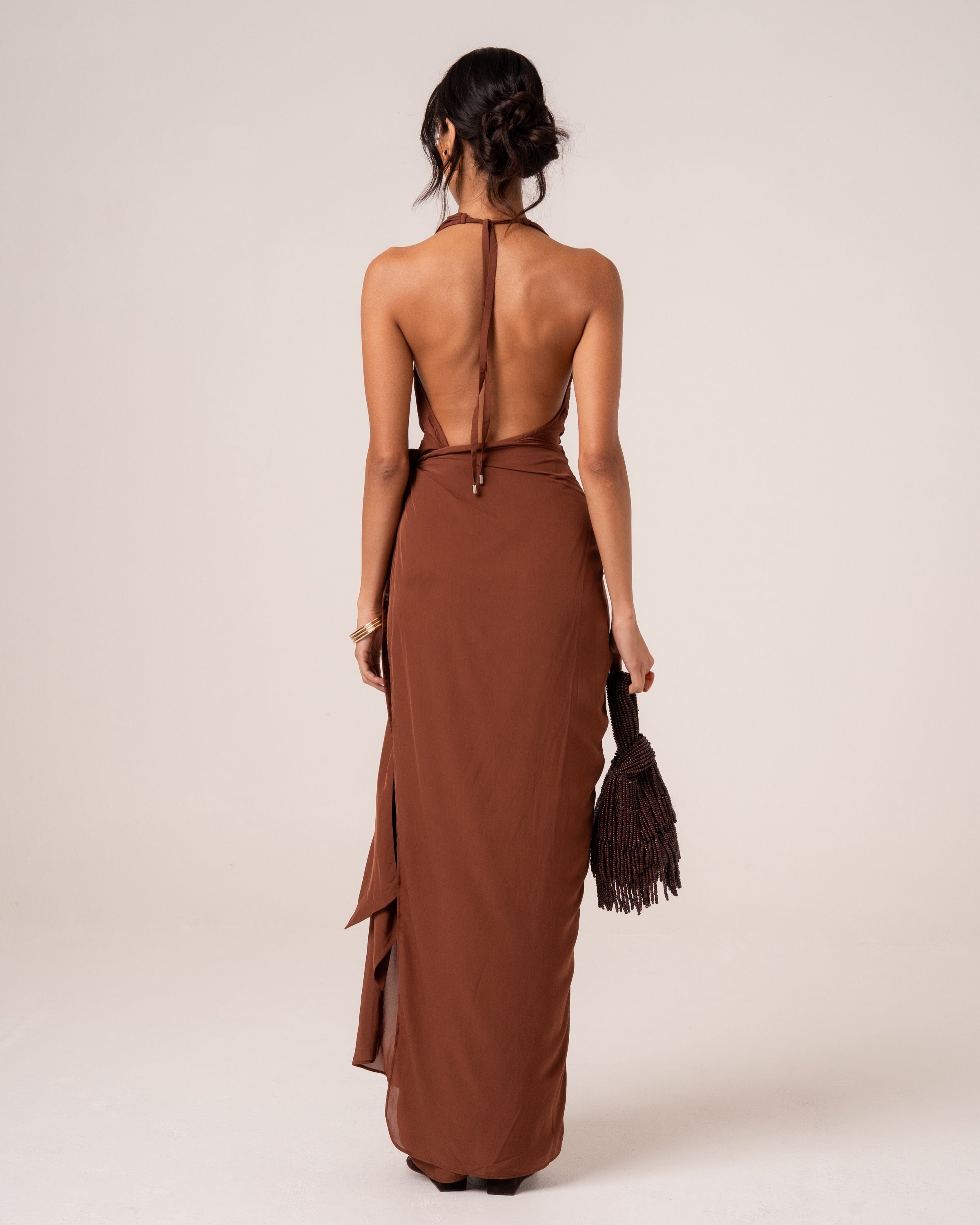 Back view of a chocolate brown halter maxi dress showing the deep open back and trailing waist tie