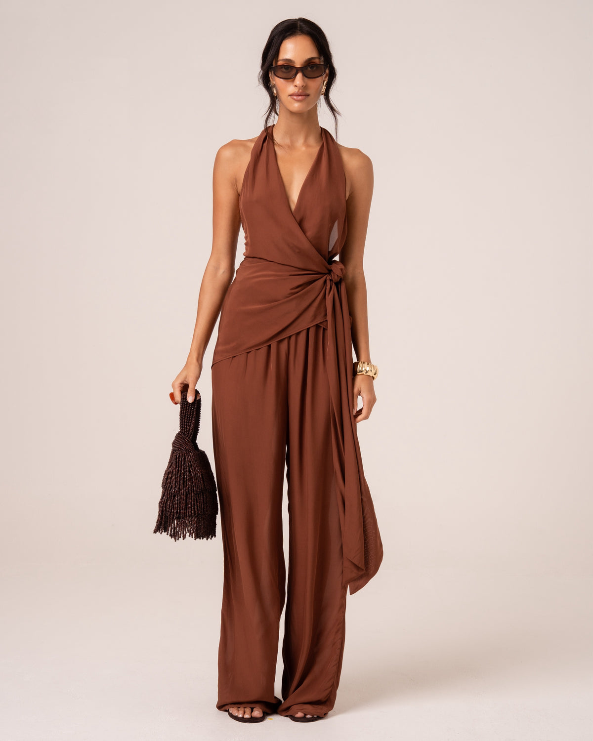 Model wearing a chocolate brown halter wrap top with a plunging neckline and knotted side tie, studio front view