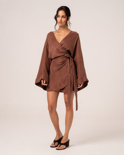 Front view of a chocolate brown batwing wrap mini dress showing the side tie waist and tulip hem, studio setting