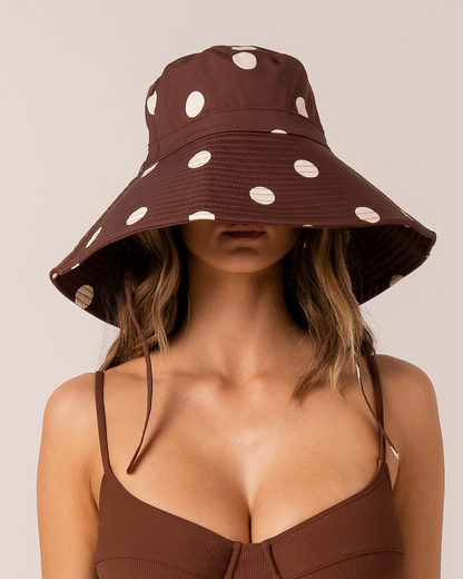 Front view of a chocolate brown polka dot cotton sun hat with a wide brim shading the model&