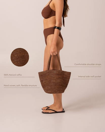 Infographic of a cocoa brown woven raffia mini tote bag on a model, highlighting comfortable shoulder straps, an internal side wall pocket, and hand-woven 100% natural raffia construction