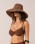 Model wearing a cocoa brown raffia bucket hat with a wide sun-shade brim, front three-quarter view with sunglasses