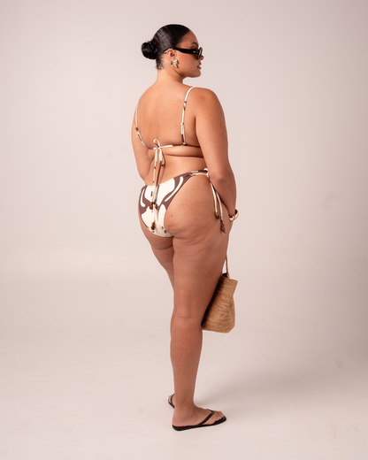 Back view of a brown and cream Ibisco floral print bikini set showing the tie-side bottom and knotted triangle top ties, studio shot