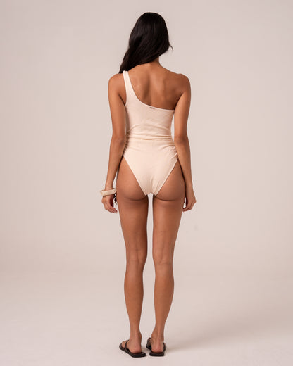 Back view of an ivory asym one shoulder one piece swimsuit showing the single shoulder strap and high-cut leg