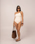 Ivory one shoulder one piece swimsuit styled with a woven raffia tote, showing the adjustable ruched side tie detail — honeymoon resortwear