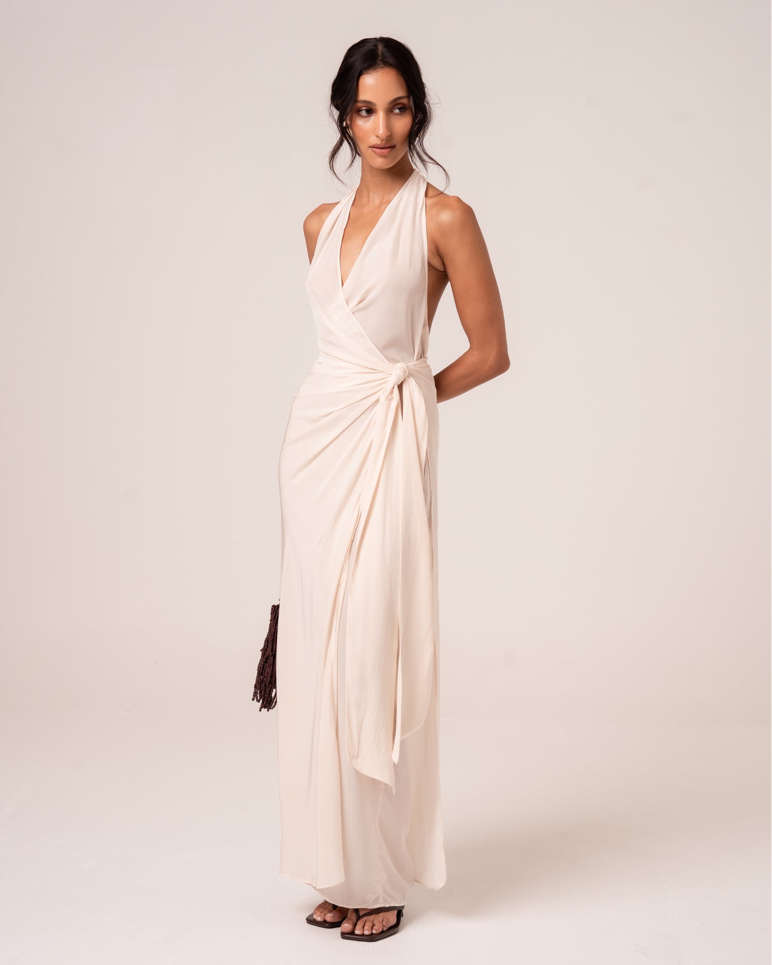 Model wearing an ivory halter wrap maxi dress with plunging neckline and knotted side tie, studio front view