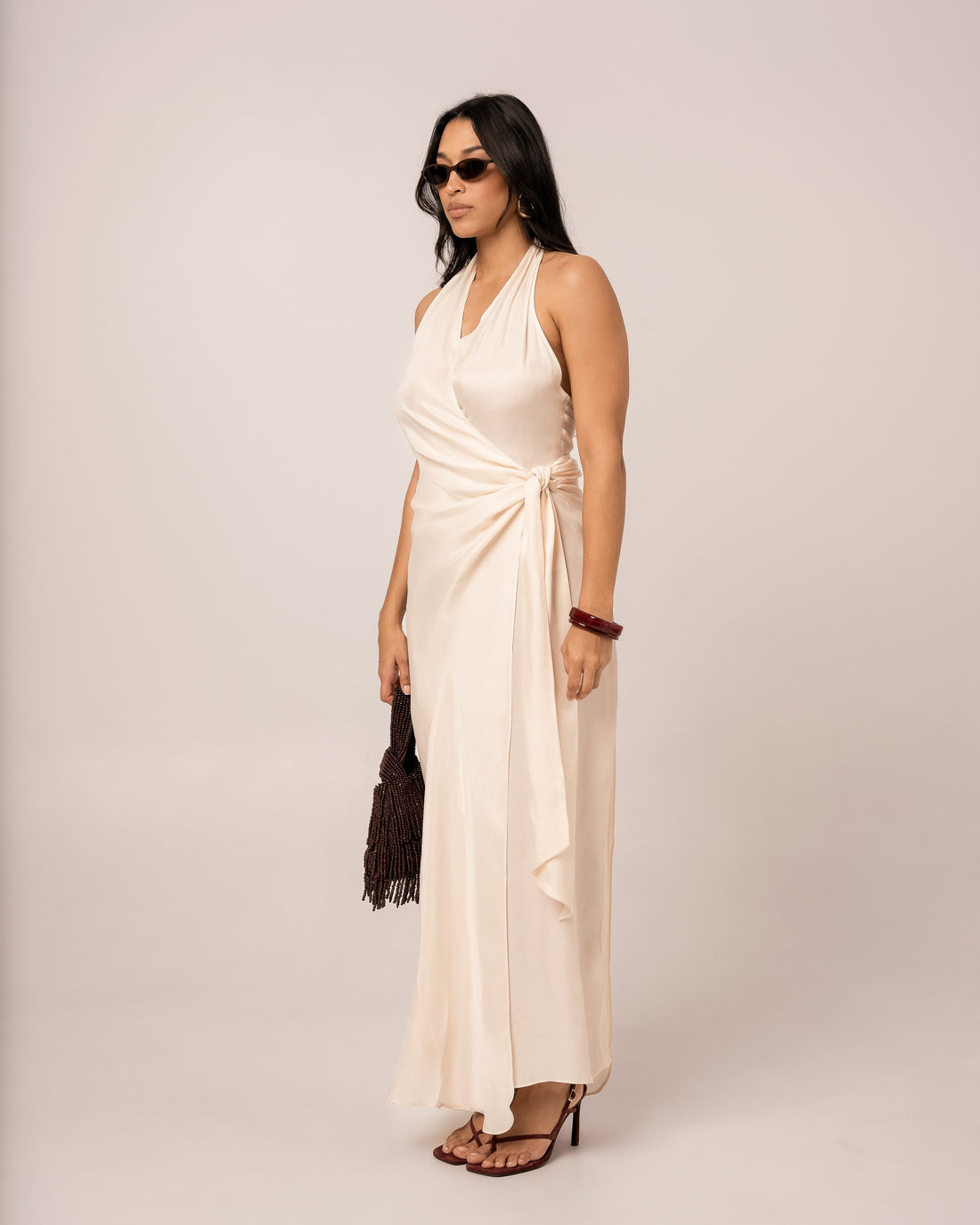 Ivory halter wrap maxi dress shown at a three-quarter angle, highlighting the draped waist knot and floor-length column skirt
