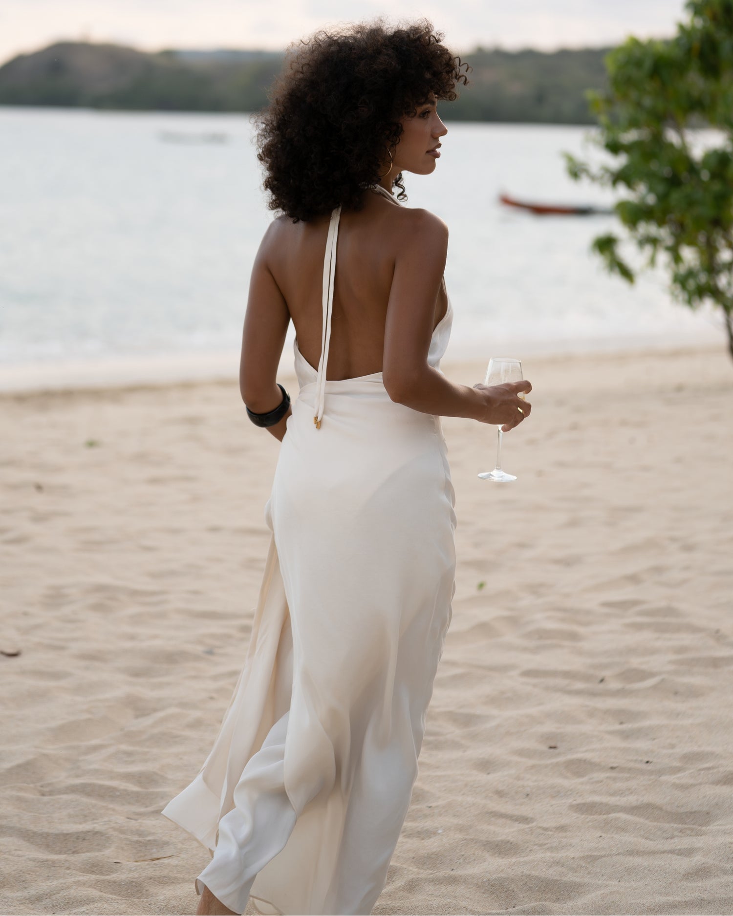Open back of an ivory halter wrap maxi dress worn beachside at dusk with a glass of wine — honeymoon resortwear