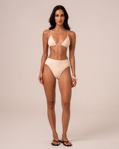 Model wearing an ivory mid rise bikini bottom with spliced panel seams and a higher leg, styled with a triangle top — studio front view