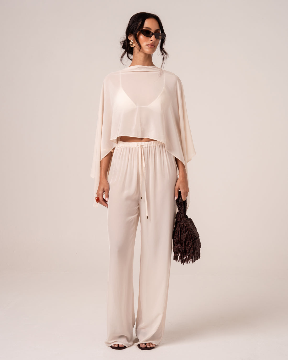 Front view of ivory viscose palazzo-style beach pants showing the gold-tipped drawstring waist, styled with a matching sheer cape