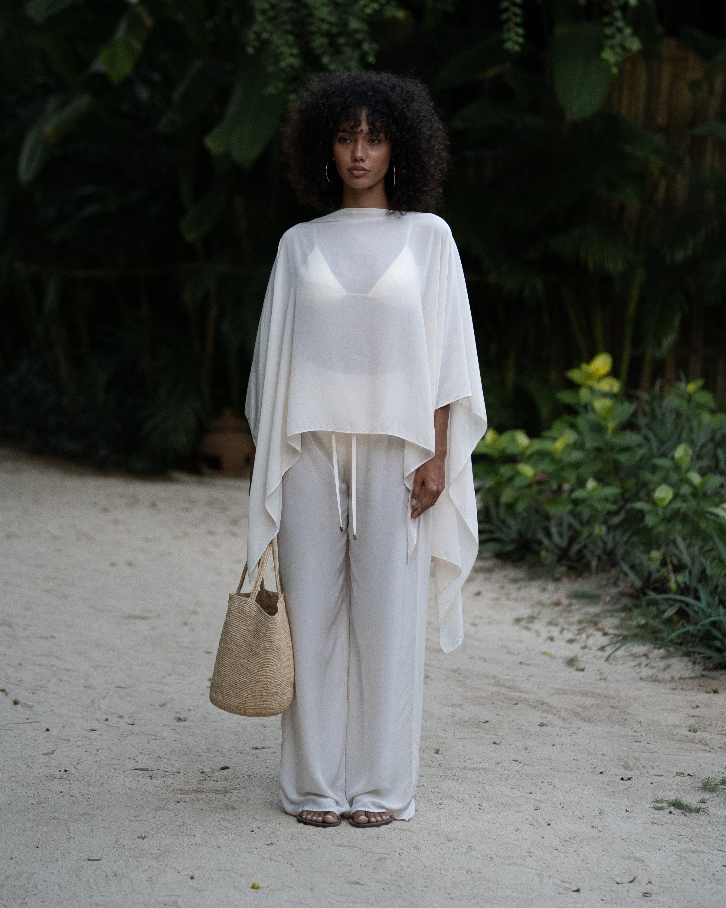 Ivory resort cape worn over a bikini top and flowy wide-leg pants on a tropical path — honeymoon resortwear by Ochre Lane